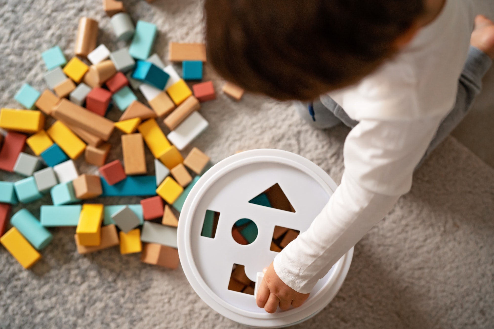 Top view of little toddler boy playing with wooden colorful building blocks sorting shapes. Child mo